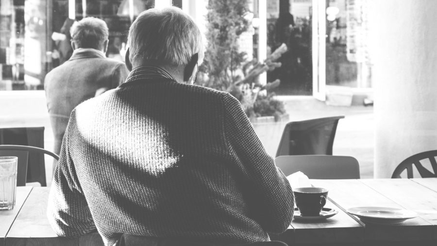An elderly man sits in cafe with his back to camera