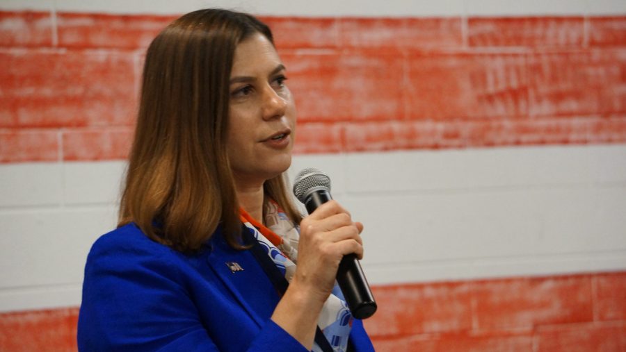 a woman in a blue blazer speaks into a microphone in front of an American flag