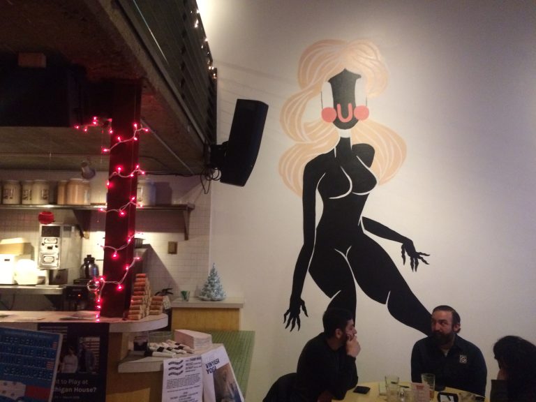 Customers sit at a table at Cass Cafe in front of artwork on the wall.