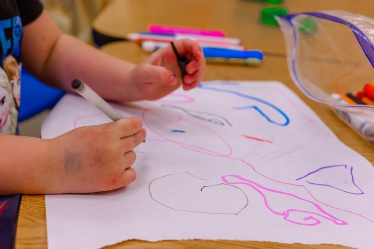 A young student uses markers and other art supplies to draw freely on a sheet of paper.