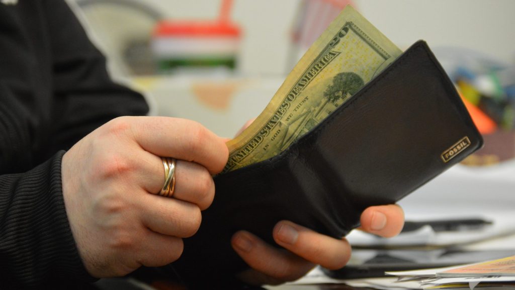 A hand pulls a $20 bill out of a wallet