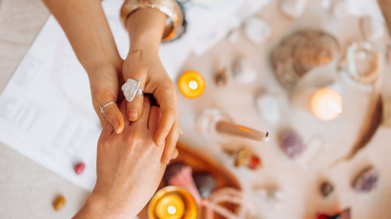 Two people hold hands with one wearing a silver ring above candles