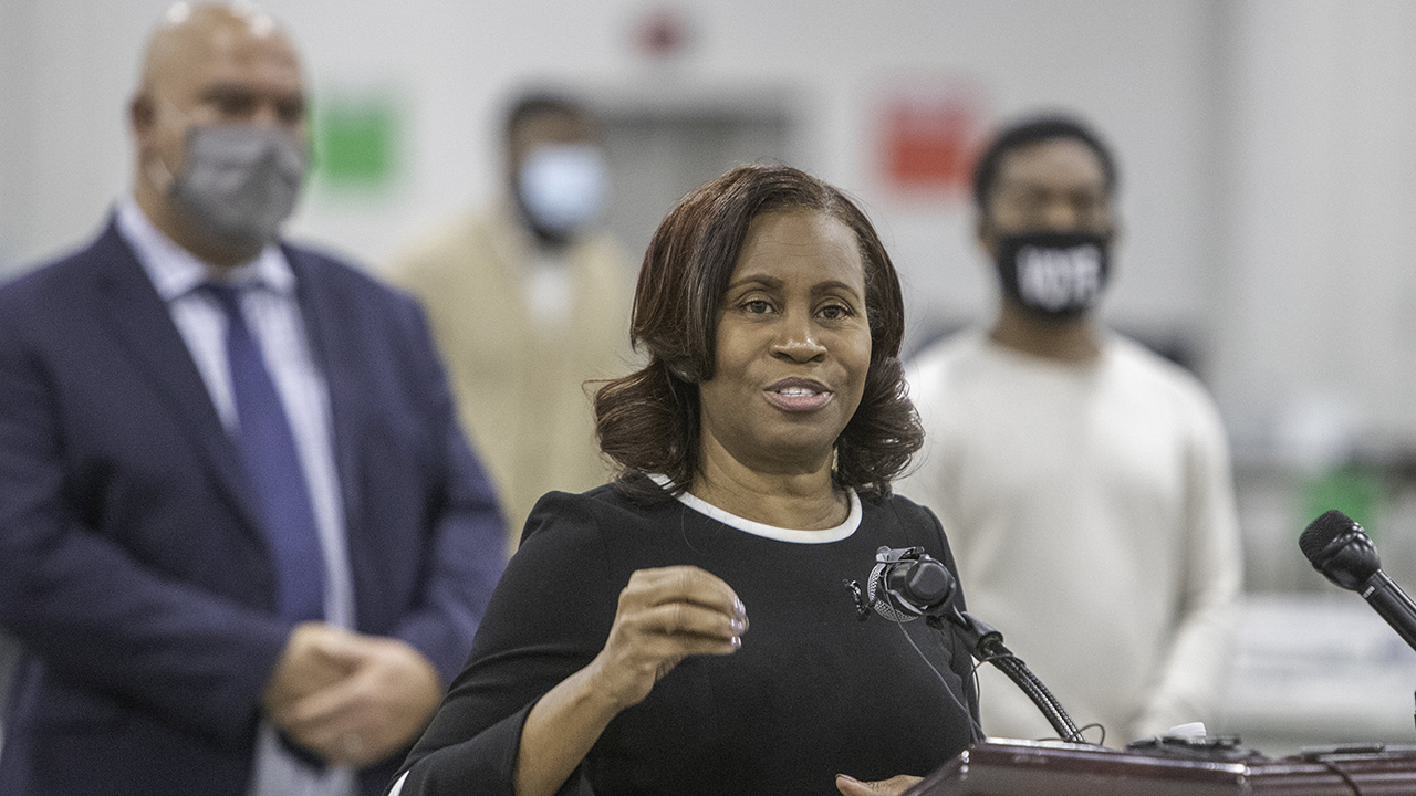 Janice Winfrey speaks at a podium wearing a black dress with a white collar.