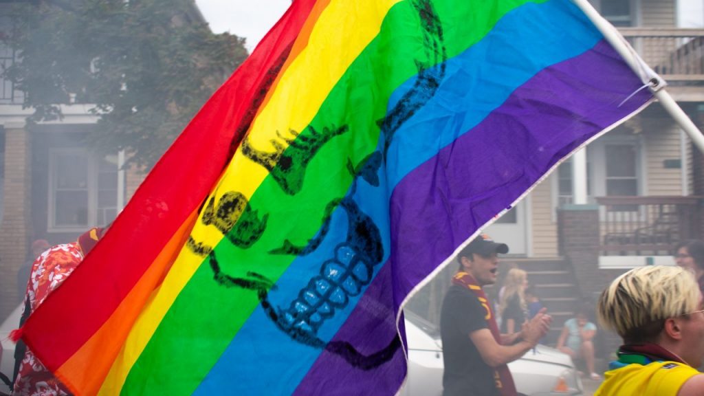 A DCFC fan wields a gay pride flag painted with the NGS logo on it, on Saturday, Aug. 13, in Hamtramck, Mich. Many NGS members will wield various LGBTQ+ flags, as NGS is, as member Chris Motzenbecker says, “We are a radically inclusive organization, we are here a hundred percent to welcome everybody into the fold. The big thing is that you support City, and you do not support hate, those are the two things that we care about.” Photo Credit: Nate Pappas/WDET