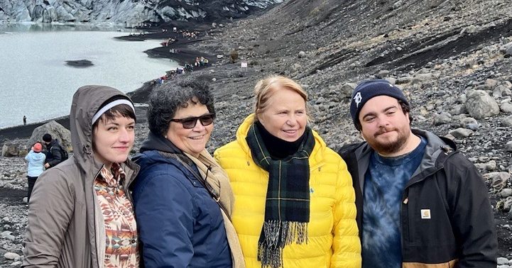 four people in coats smile in front of a pool of water, ice and land