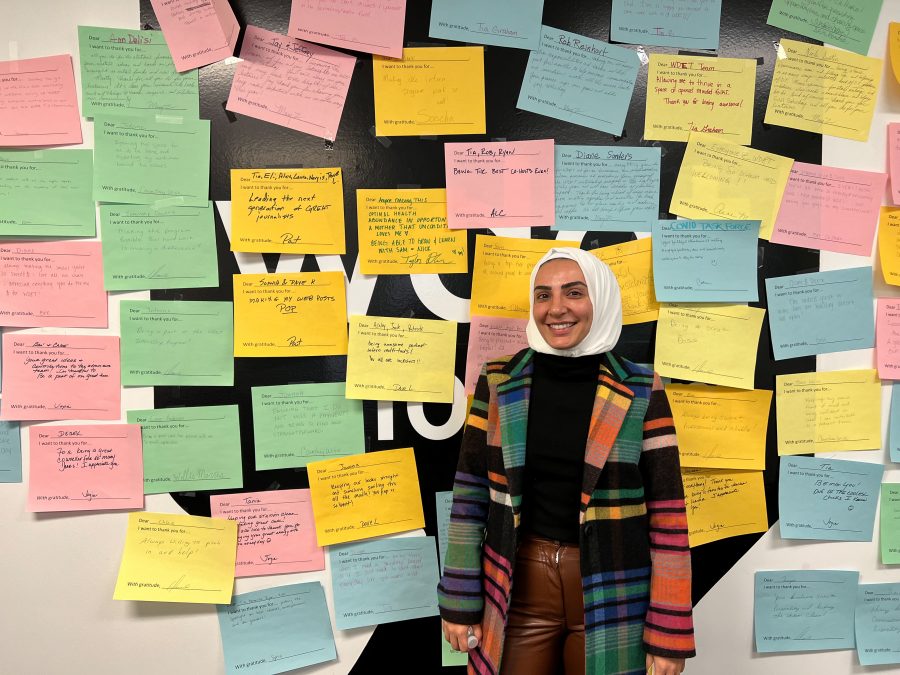 nawal alsaeed smiles in front of the WDET logo (which is covered with multi-colored notes of appreciation from WDET staff) at our studios