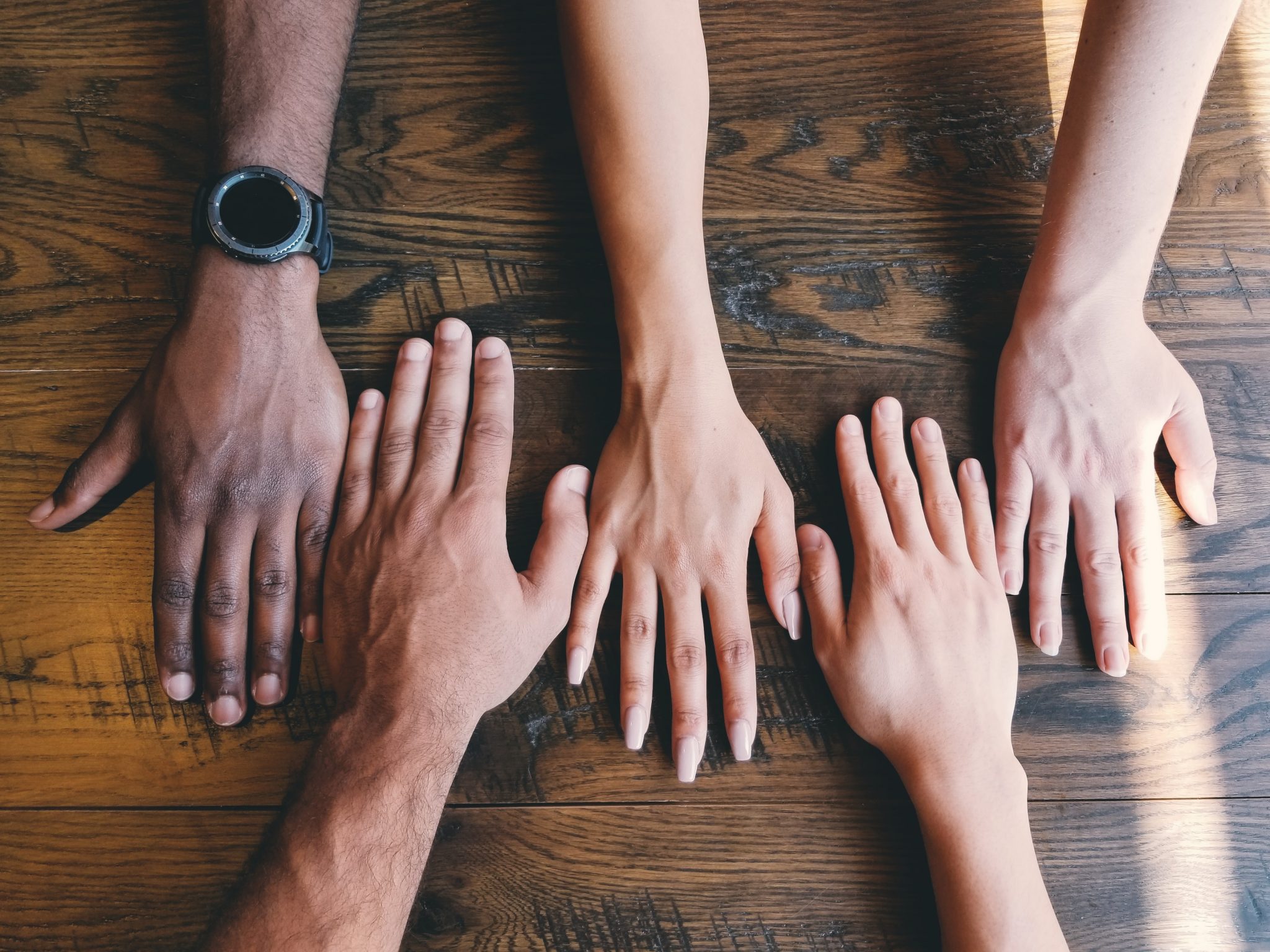 Hands of varying skin tones are on a table.