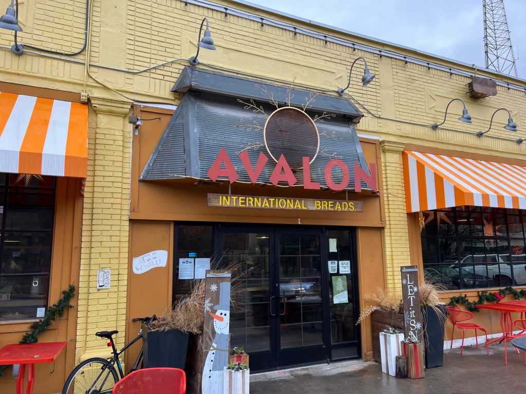 exterior of yellow brick building with a red sign that reads "Avalon International Breads"