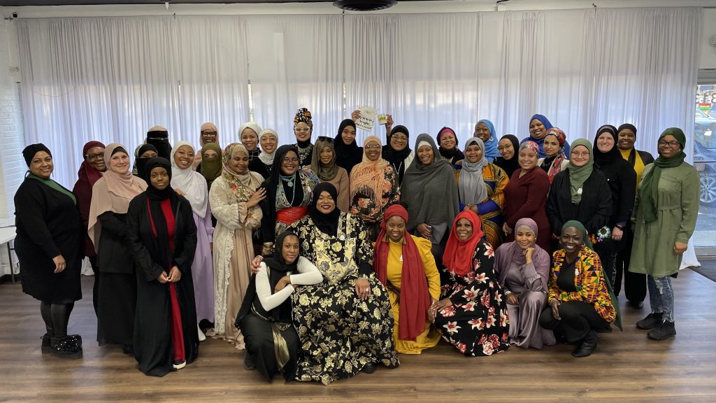 A large group of hijabi women pose for a picture in a meeting space