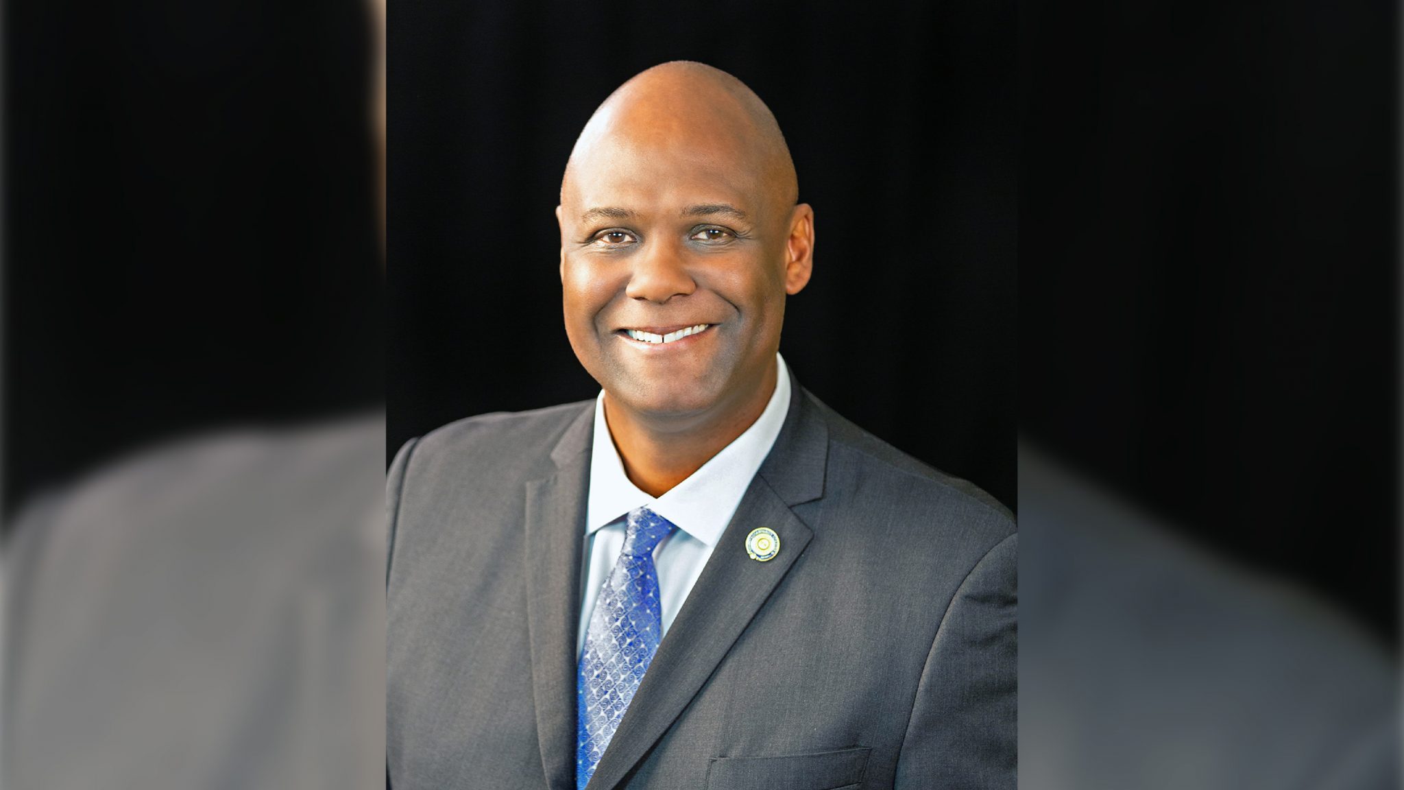 headshot of a Black man in a gray suit and a blue tie