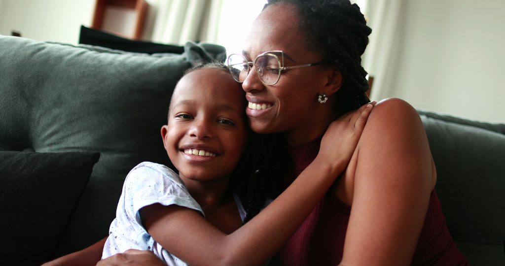 A Black mother and child smile and embrace on the couch