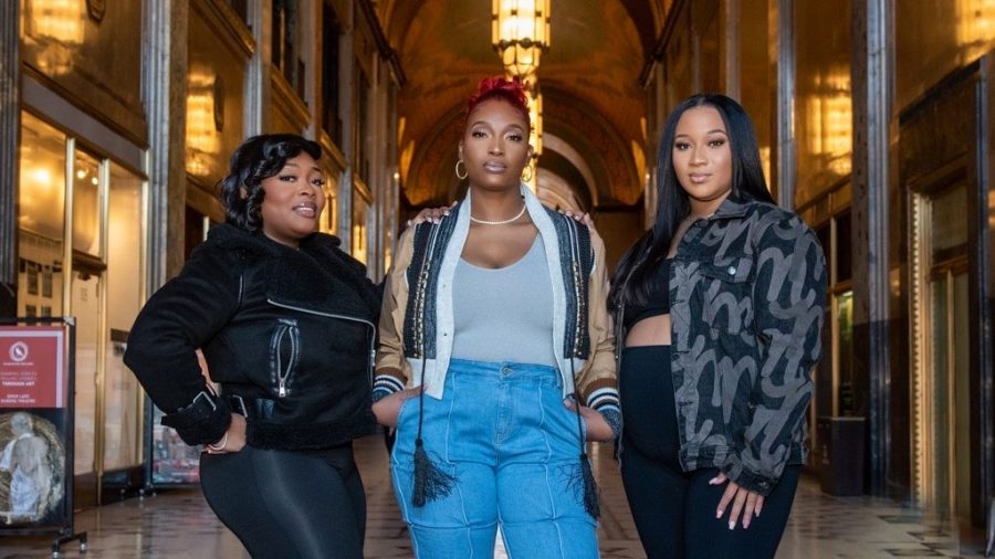 Three Black women pose in fashionable clothing.