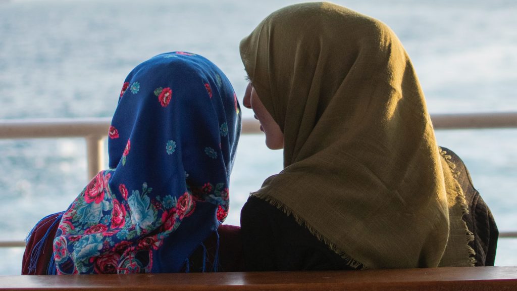 Women wearing hijab headdress sitting on a bench.