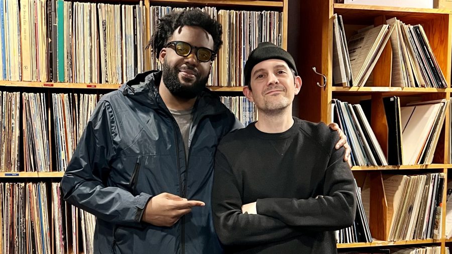 two men pose in front of a record collection