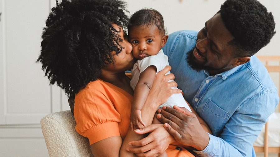 Photo of Black mother and Black father holding their child.