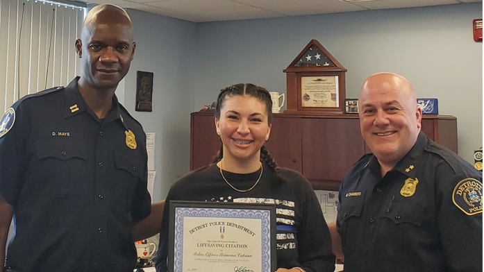 Three police officers smile with the middle one holding a certificate