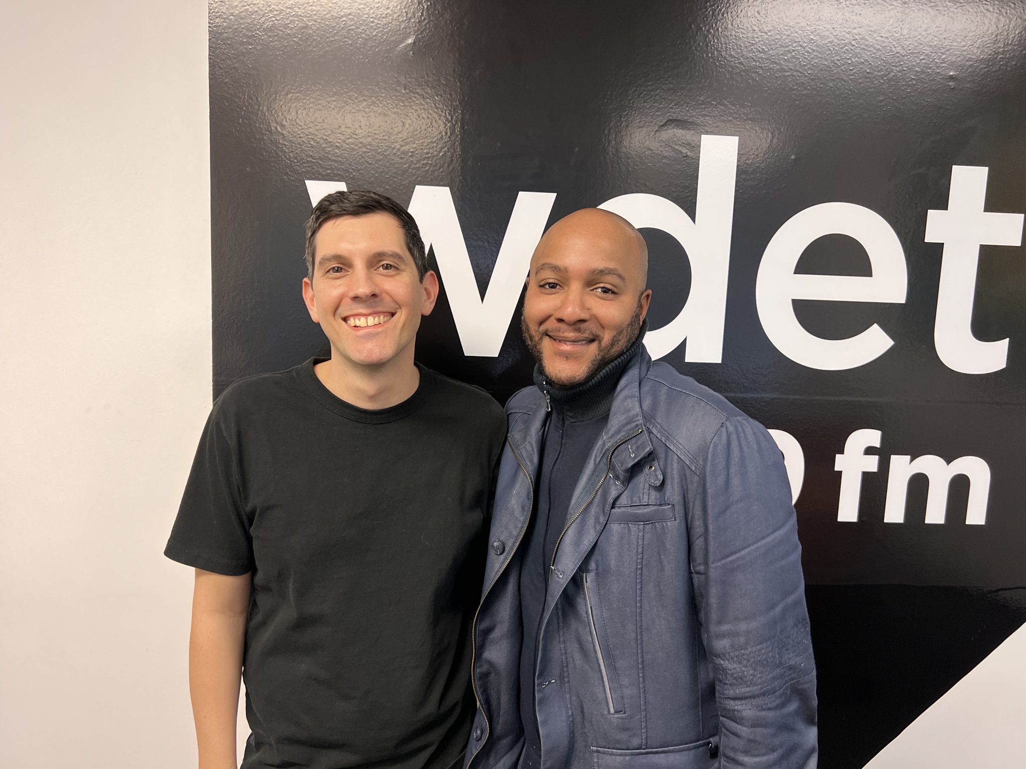 Sam Beaubien and Jon Dixon smile in front of the WDET logo