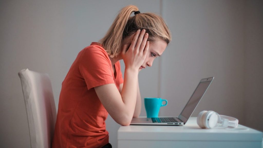 Woman placing her hands to her head while staring at her laptop.