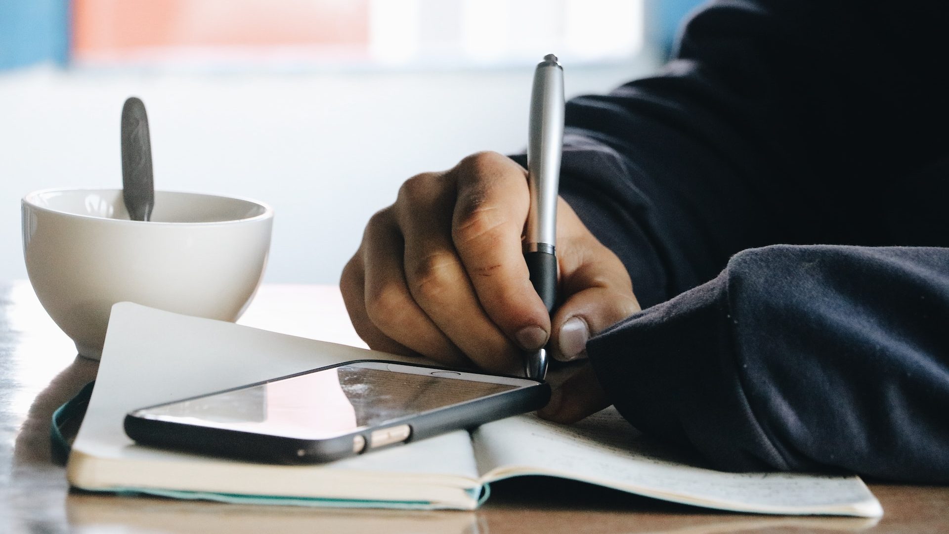 Person writing in a notebook with their phone out