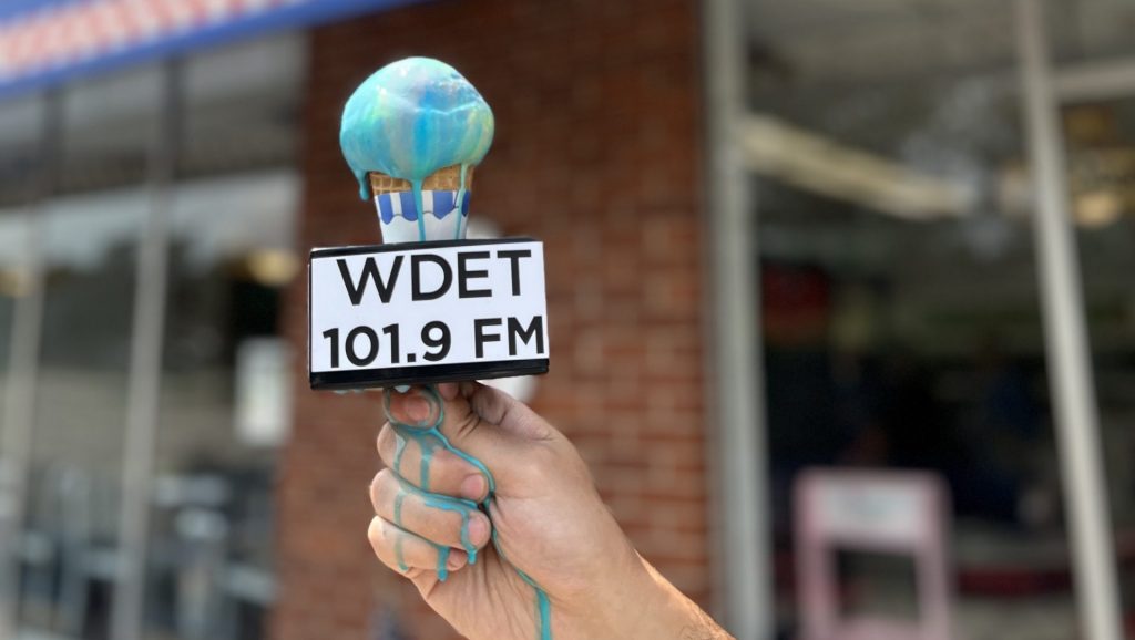 A cone of Superman ice cream with a WDET microphone flag melts down a reporters hand.