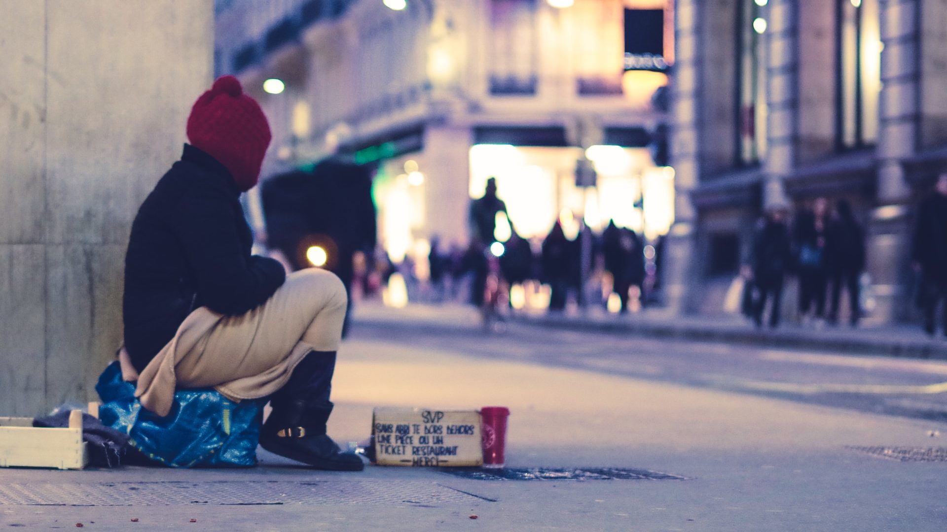 Homeless person sits on sidewalk.