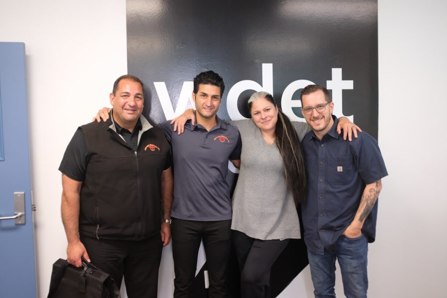 Emmet and Gino Baratta smile with Ann Delisi and James Rigato in front of WDET's logo