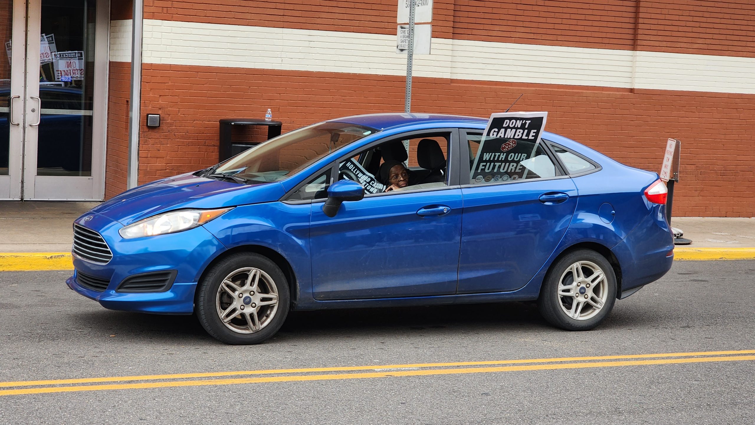 A car drives past a picket line with pro-union signs hanging out the window.