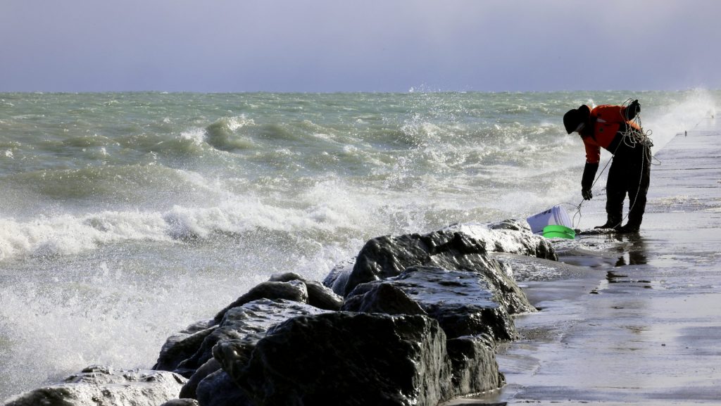 Rae-Ann Eifert, a lake monitor for the Wisconsin Department of Natural Resources, braved sub-freezing temperatures to gather buckets of water for testing off a Lake Michigan breakwater in Racine, Wis., on Feb. 28, 2024, as part of an effort across the Great Lakes to understand the effects of an iceless winter.