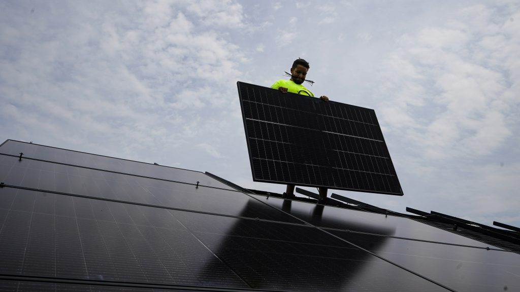 Nicholas Hartnett, owner of Pure Power Solar, holds a panel as his company installs a solar array on the roof of a home in Frankfort, Ky., July 17, 2023.