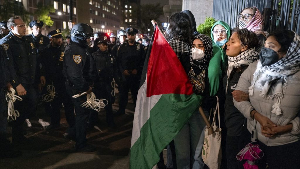 Demonstrators hold their ground near a main gate at Columbia University in New York, Tuesday, April 30, 2024, as New York City police officers move to clear the area after a campus building was taken over by protesters earlier in the day.