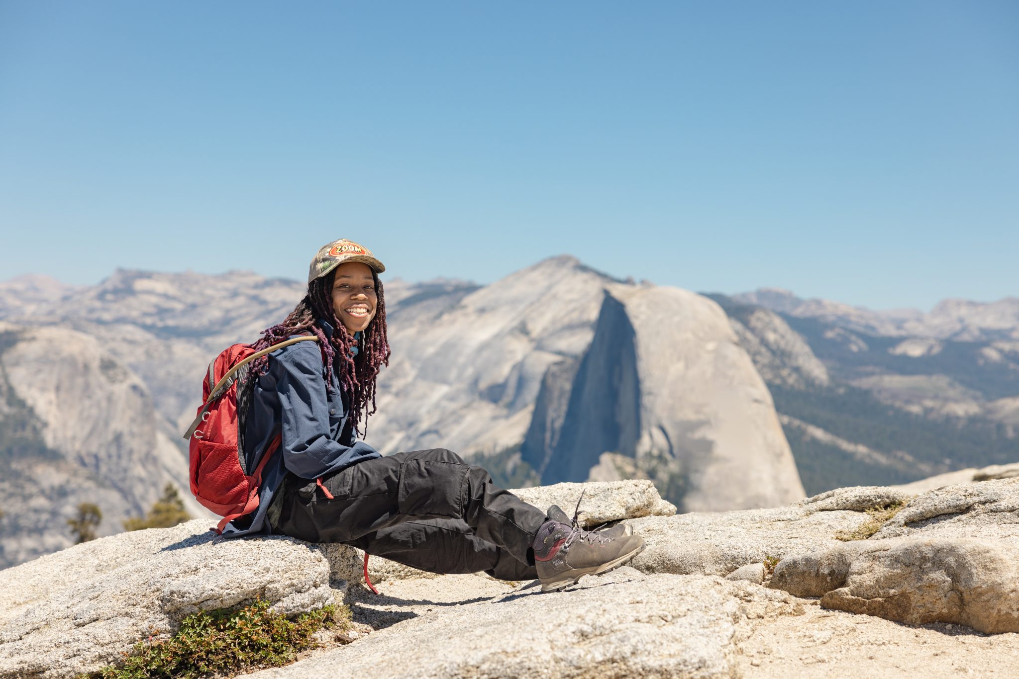 Young African American woman smiles as she sits on rock with mountains stretching in the background