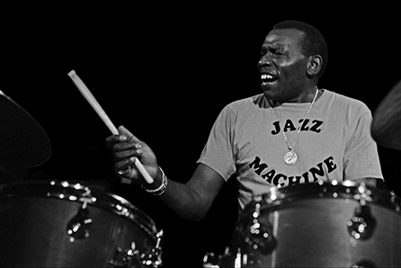 Elvin Jones plays drums wearing a shirt that says "Jazz Machine"