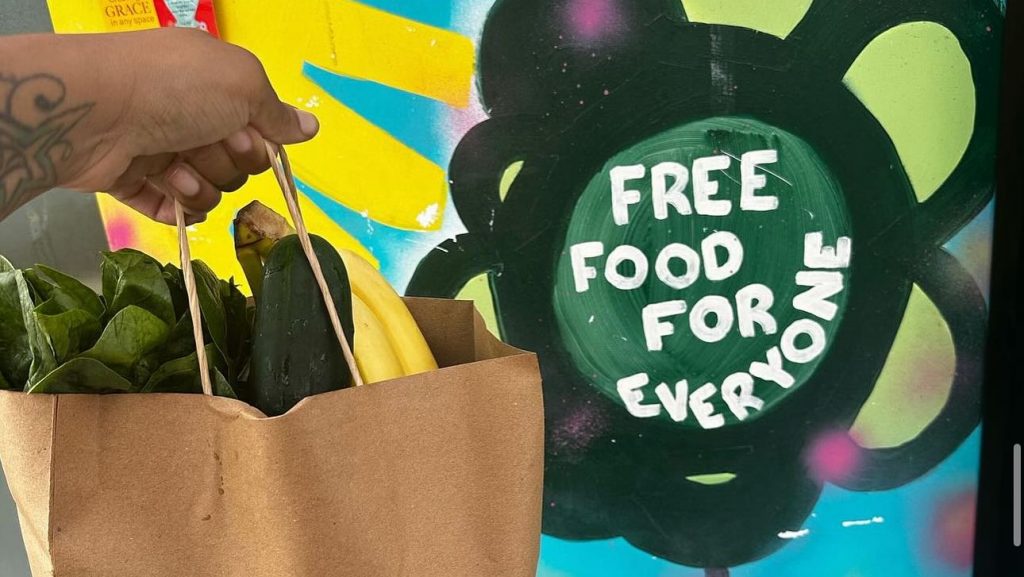 A brown bag of produce in front of a mural that reads, "Free food for everyone"