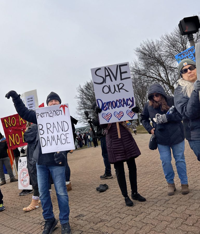 Tesla Takedown protestors demonstrate on the sidewalk outside Somerset Mall in Troy.