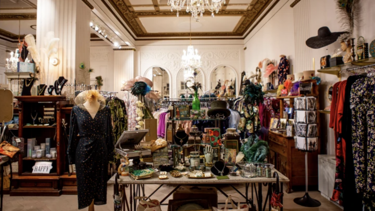 The floor of The Peacock Room Boutique is rife with vintage treasures. Tables are covered with jewelry displays and a fashionable mannequin stands with a dark patterned evening dress. A chandelier hangs from the ceiling.