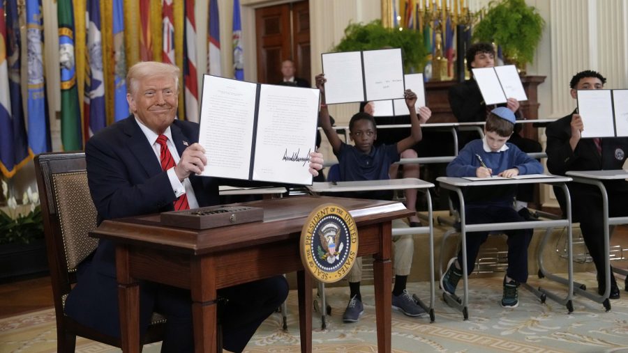 President Donald Trump, left, holds up a signed executive order as young people hold up copies of the executive order they signed at an education event in the East Room of the White House in Washington, Thursday, March 20, 2025.