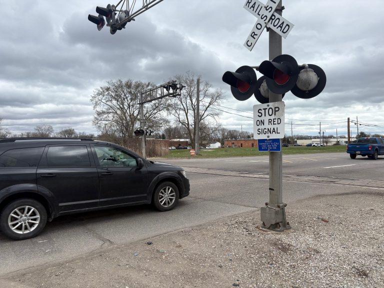 A car sits at a railroad crossing.