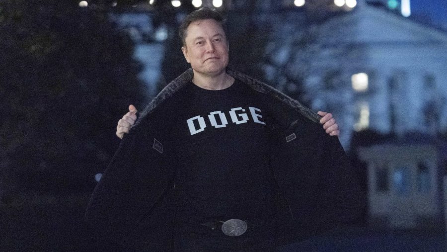 Elon Musk flashes his t-shirt that reads "DOGE" to the media as he walks on South Lawn of the White House, in Washington, Sunday, March 9, 2025.