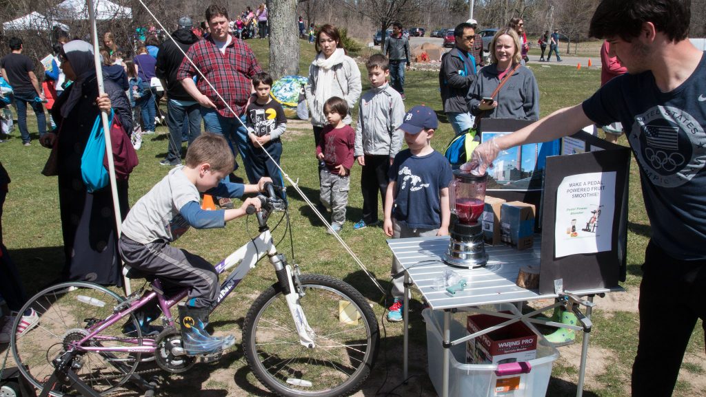 A kid riding a bike that powers a blender at an Earth Day event