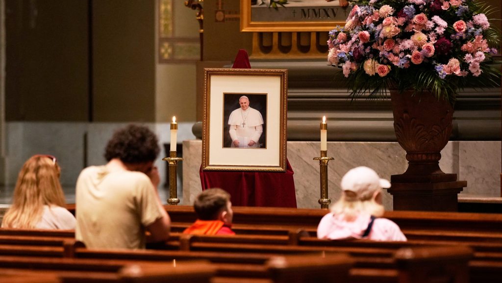 People pray near a picture of Pope Francis inside the Cathedral Basilica of Saints Peter and Paul, Monday, April 21, 2025, in Philadelphia.