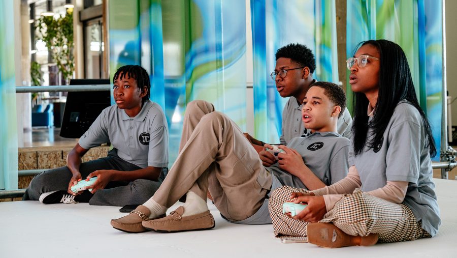 Four teens in school uniforms playing a video game