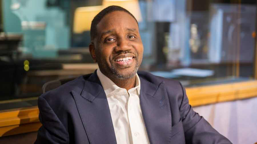 Detroit Pastor Solomon Kinloch Jr. smiling and sitting in the WDET studios in a blue suit.