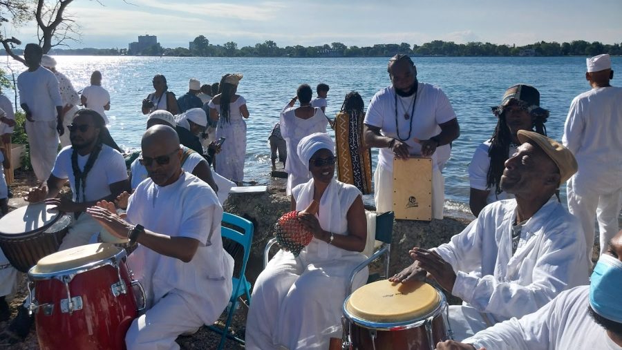 A group of people dressed in white play drums along the Detroit River
