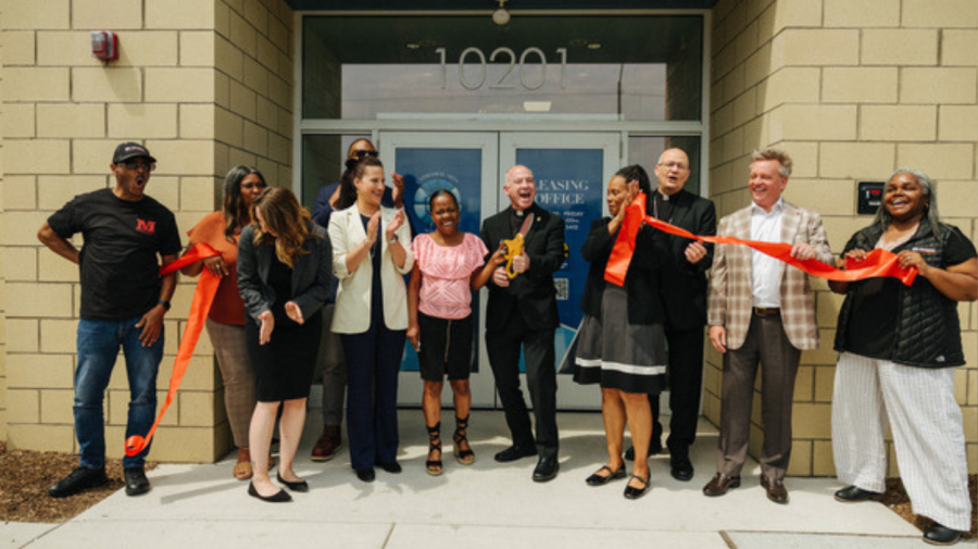 A group of people in front of a building holding a ribbon that has been cut.