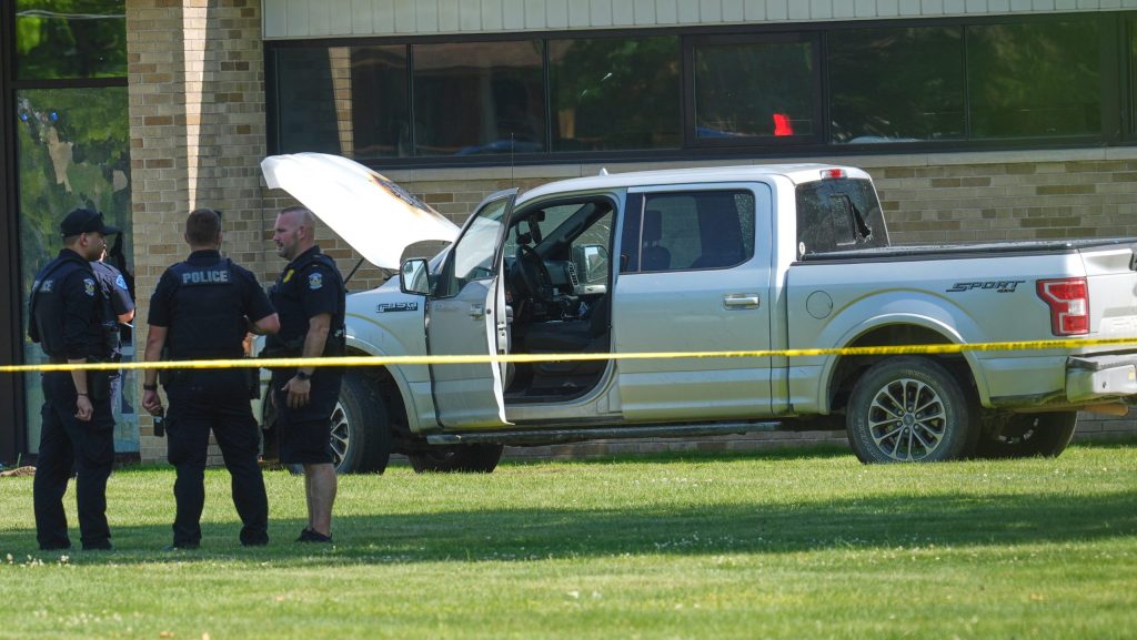Police walk by an idle vehicle near CrossPointe Community Church in Wayne, Mich., Sunday, June 23, 2025.