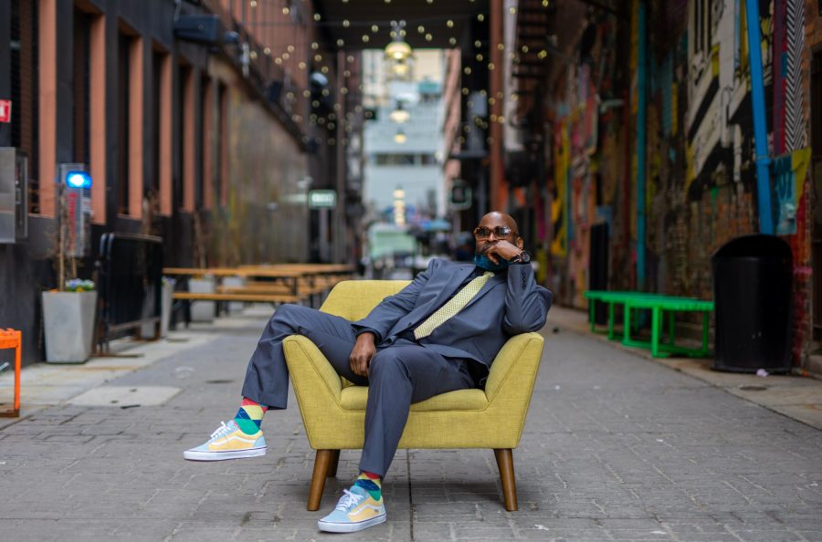 Dean Beanz sits in an upholstered chair in an alley way.