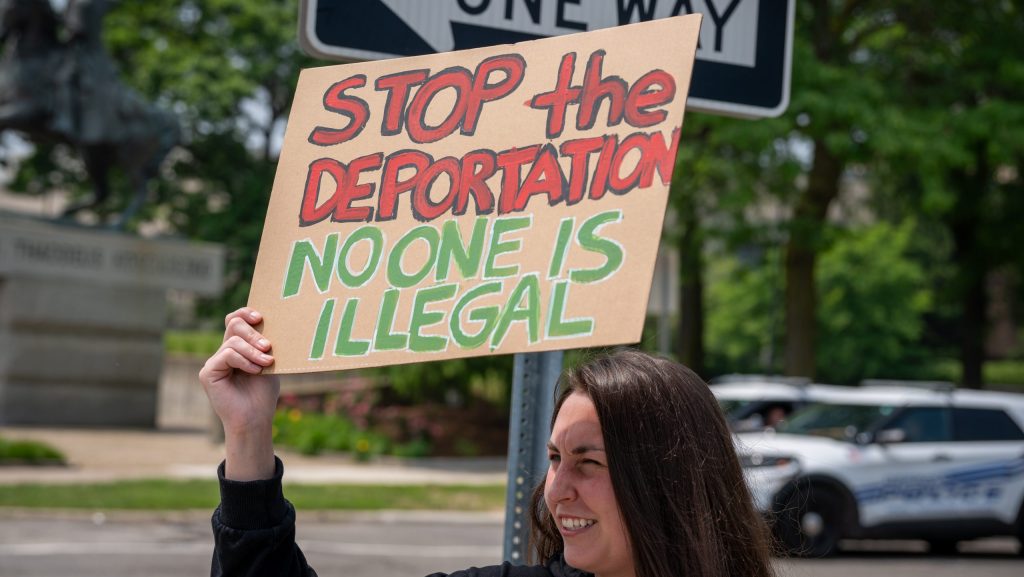 A demonstrator holds up a handmade sign that says "Stop the deportation No one is illegal"