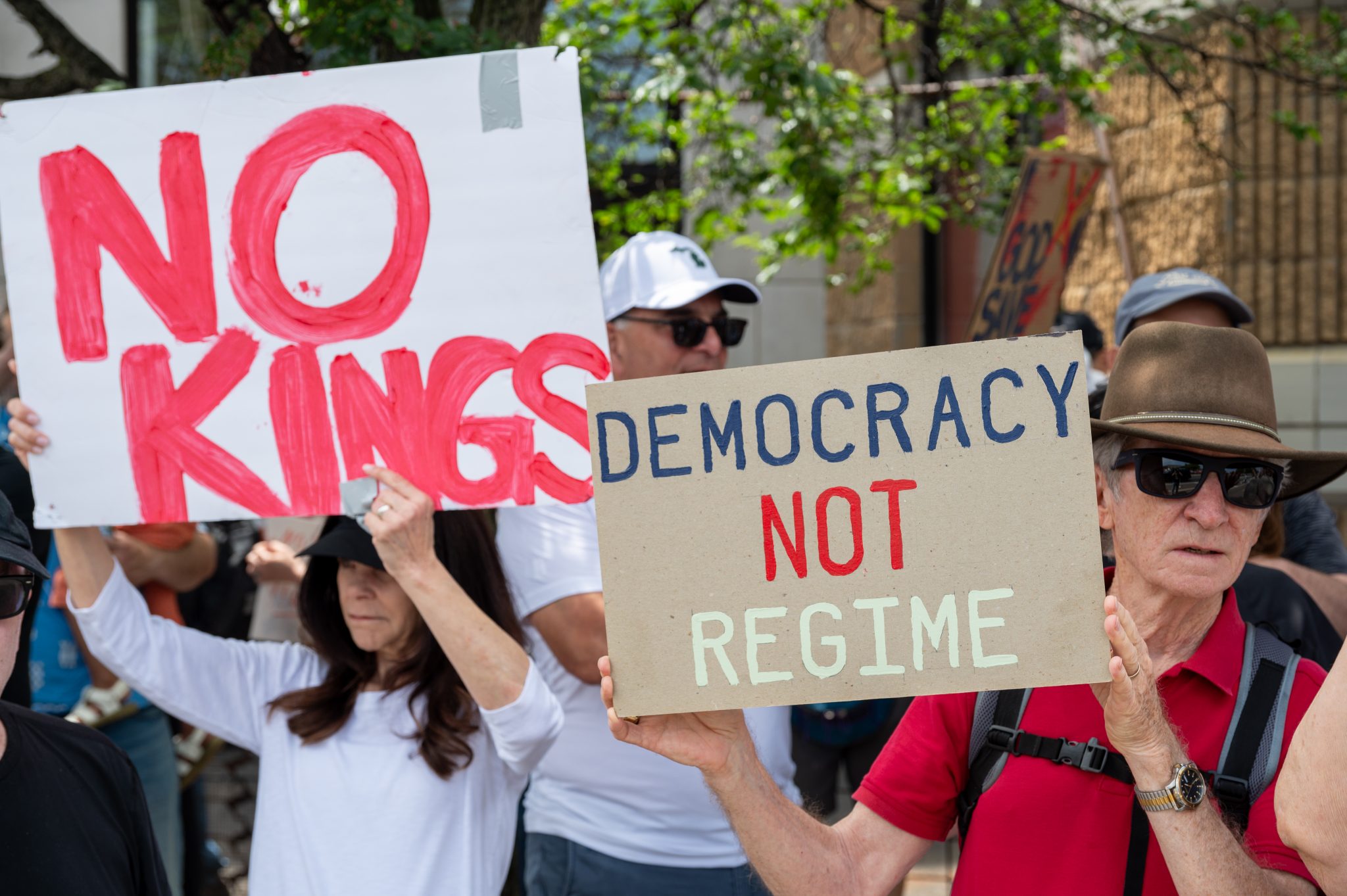 Protesters hold hand-made signs that say, "No kings" and "Democracy, not regime"