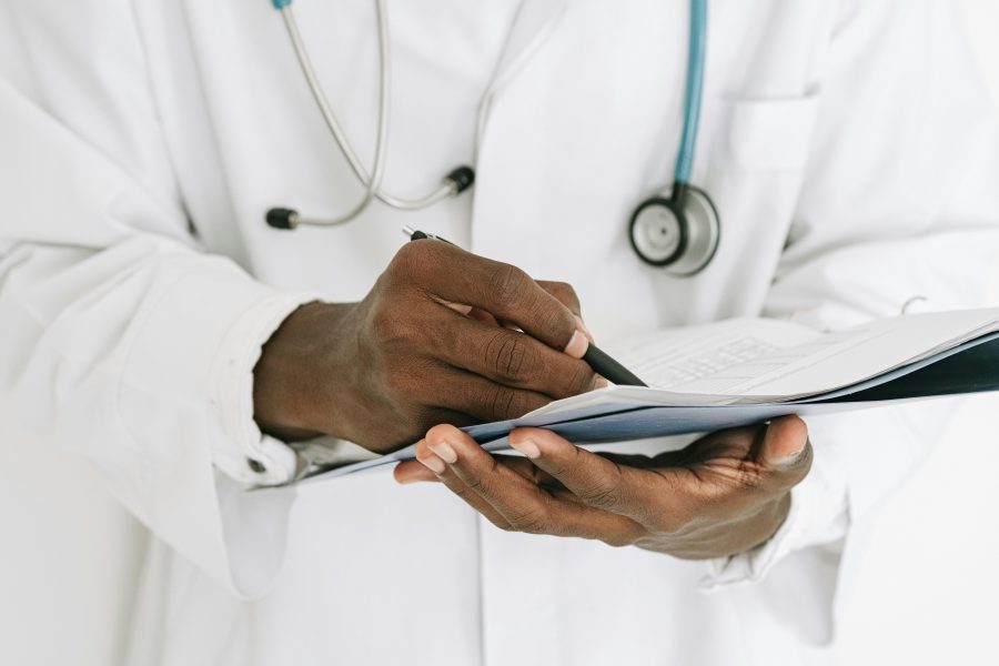 A male doctor holds a patient file. He's wearing white coat.