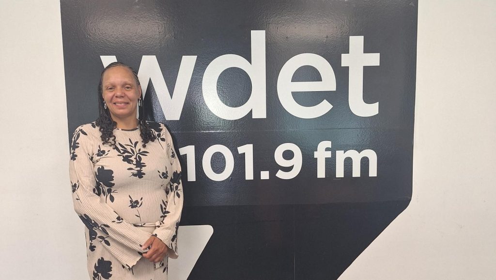 DaNetta Simpson poses in front of the WDET logo